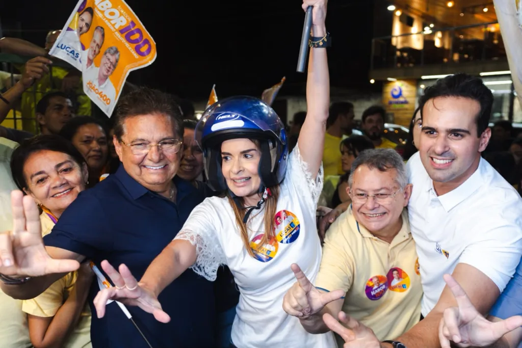 Lucas Ribeiro posa ao lado de Daniella Ribeiro com capacete de moto e de Adriano Galdino cercados por militantes.