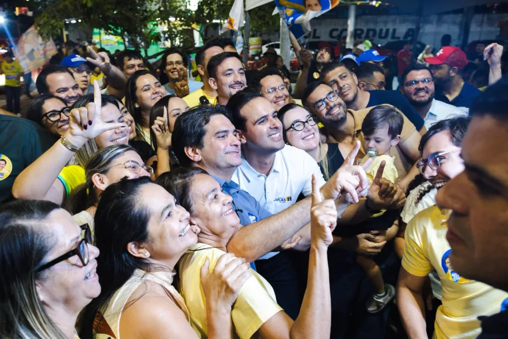 Lucas Ribeiro posa sorridente para selfie ao lado de Murilo Galdino e grupo de militantes.
