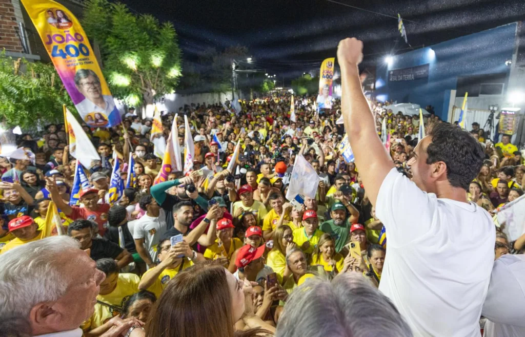 Lucas Ribeiro ergue o punho fechado em saudação a uma grande massa de eleitores com bandeiras em Cajazeiras.