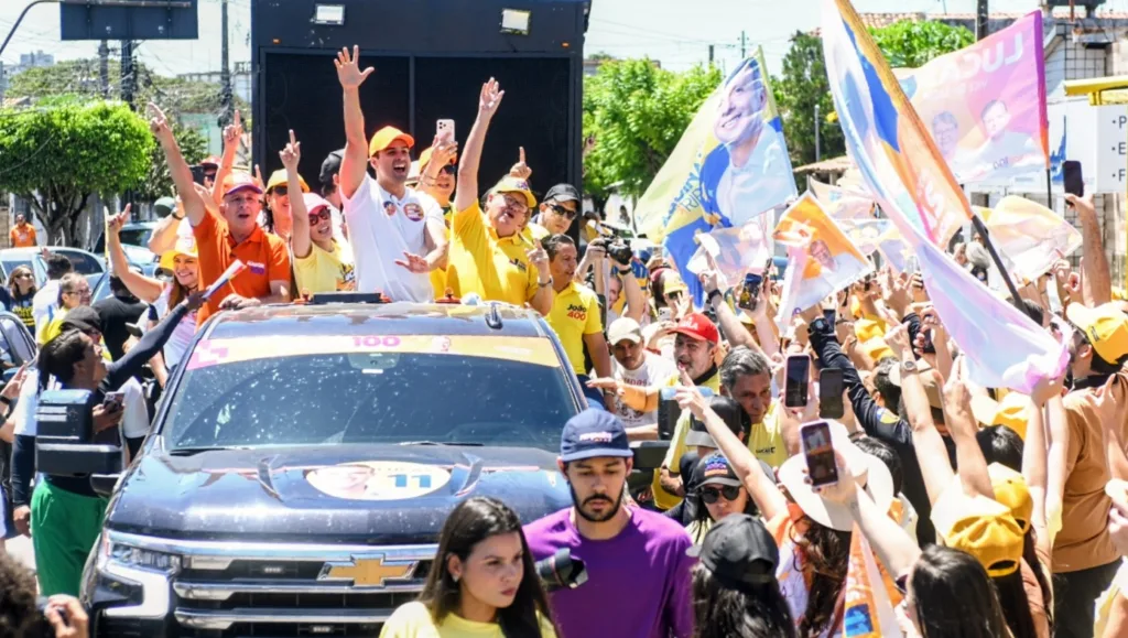 Veículo de campanha com Lucas Ribeiro, João Azevêdo e lideranças com braços erguidos cercado por multidão de apoiadores.